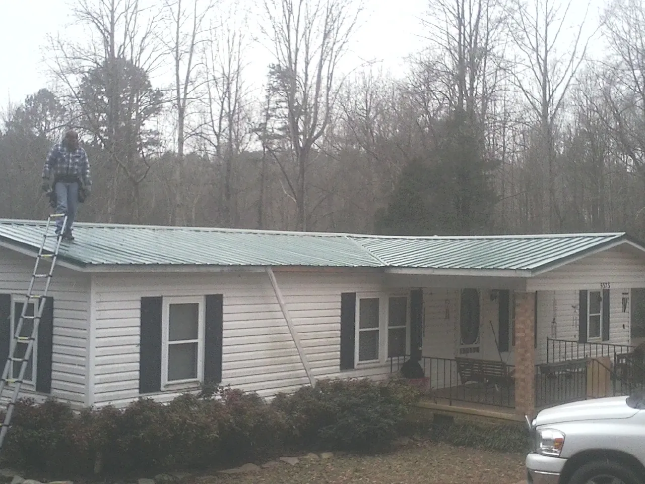Worker on a ladder beside a new green metal roof on a ranch home in Burlington